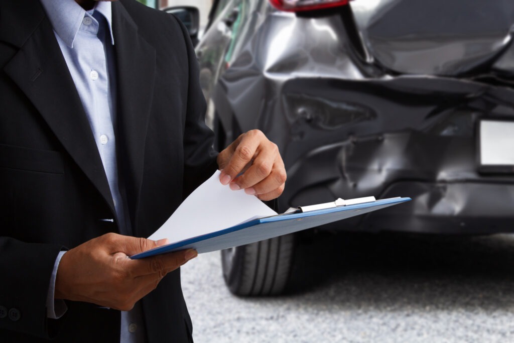 An insurance agent in a suit with a clipboard sizing up the damages of a car accident.