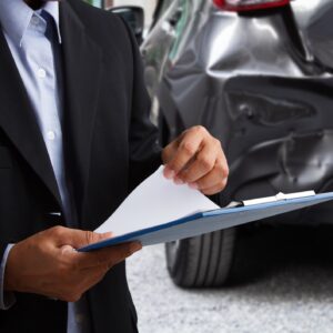 An insurance agent in a suit with a clipboard sizing up the damages of a car accident.