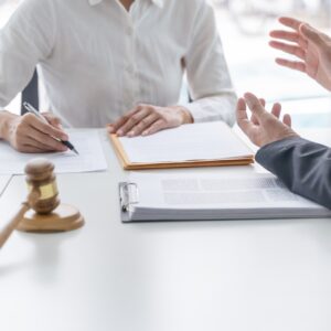 A lawyer sitting across from their client at a white table discussing a potential lawsuit.