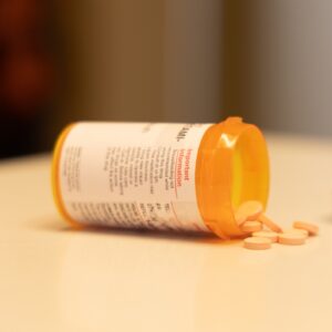 An orange pill bottle on its side with white pills spilling out onto the table.