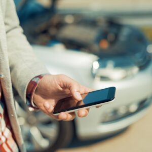 a man in a grey sweater and flannel using his smartphone next to his totaled grey car.