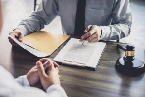 A lawyer sharing important documents across from his client on a wooden desk.