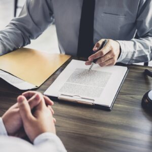 A lawyer sharing important documents across from his client on a wooden desk.