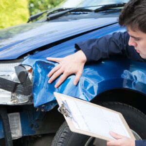 Insurance adjuster taking a look at a blue totaled car inspecting the damage.