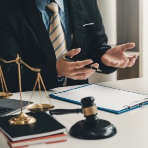 A lawyer in a navy suit and tie discussing a complex topic to their client across from their white wooden desk.