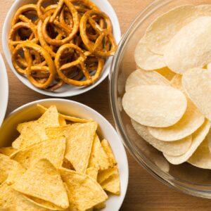 Four glass bowls -- three filled with different types of potato chips and one filled with pretzels.